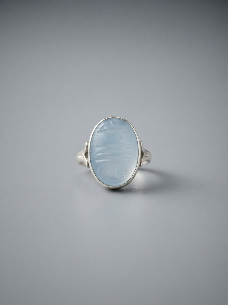 Ein massiver Herrenring aus 925er Sterlingsilber mit kunstvollen Verzierungen an den Seiten. Im Zentrum sitzt ein großer, oval geschliffener, transparenter Dur-e-Najaf-Quarzstein. Auf der flachen Oberseite des gläsernen Steins ist in feiner arabischer Handkalligrafie 