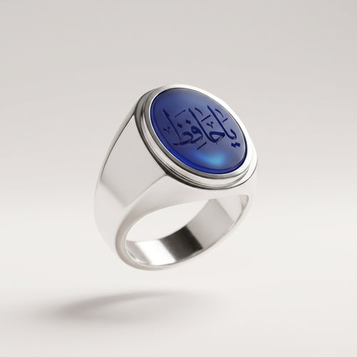 Polierter, glatter Siegelring aus massivem 925 Feinsilber mit einem hochgewölbten, ovalen blauen Aqīq-Cabochon und der handgravierten arabischen Bittschrift 'يا حافظ' (Ya Hafiz), schwebend in 3/4-Seitenansicht auf hellem Studio-Hintergrund.