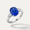Saphir Trilogie Ring «Bleu Royal» aus massivem, rhodiniertem 925 Feinsilber, schwebend in 3/4-Ansicht mit einem leuchtend blauen ovalen Saphir und zwei trapezförmigen Baguette-Diamanten an den Flanken auf hellem Studio-Hintergrund.